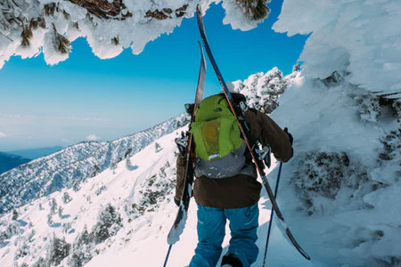 A person is hiking the side of a mountain with skis on their back.